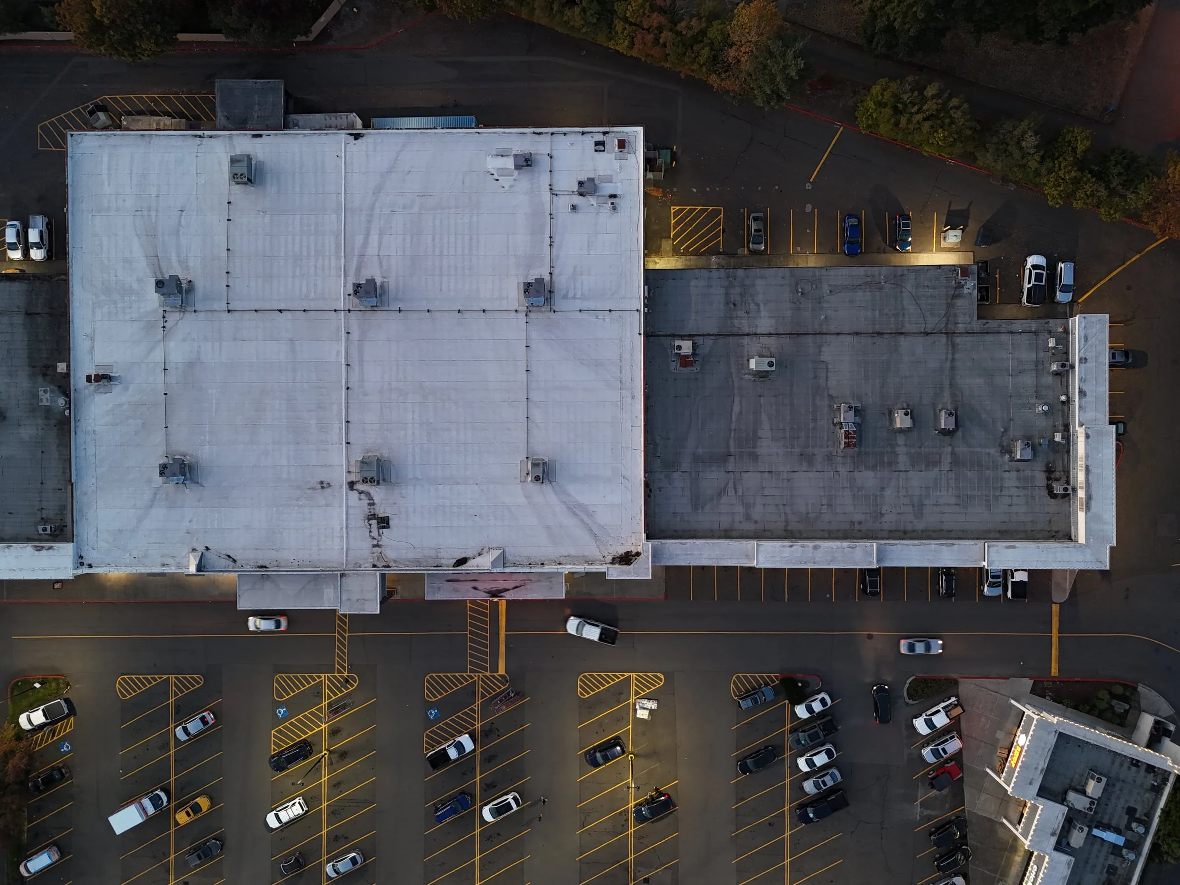 A commercial flat roof seen from above at dusk, with the parking lot lights on.