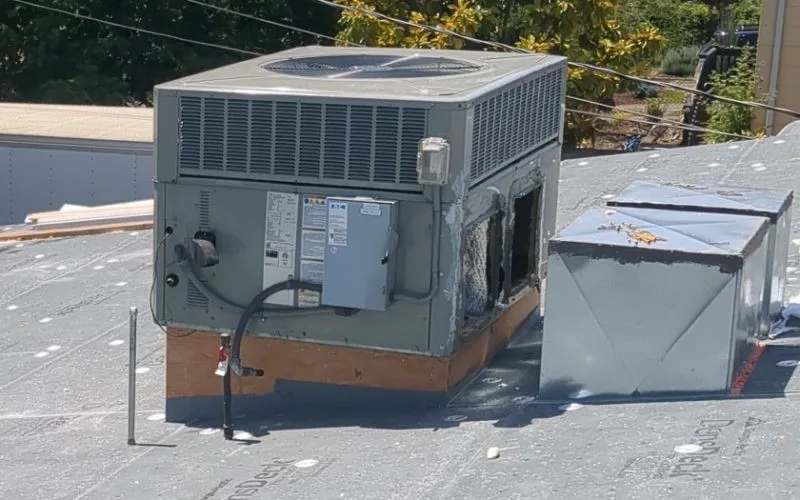 Grey DensDeck cover boards fastened across a flat roof with rows of round metal plates, running right up to a rooftop HVAC unit on a wood curb, before the membrane is installed