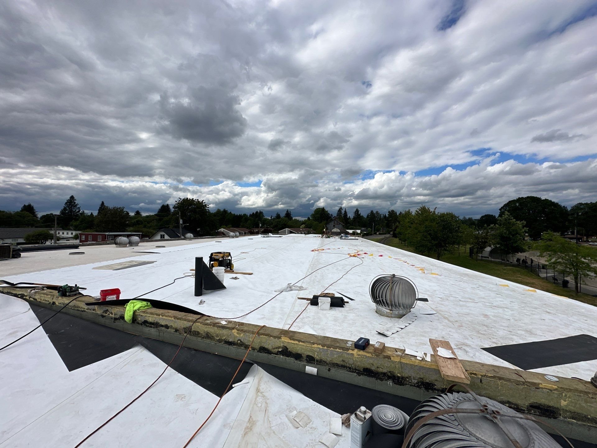 A commercial reroof in progress under a stormy sky, the new white membrane nearly complete