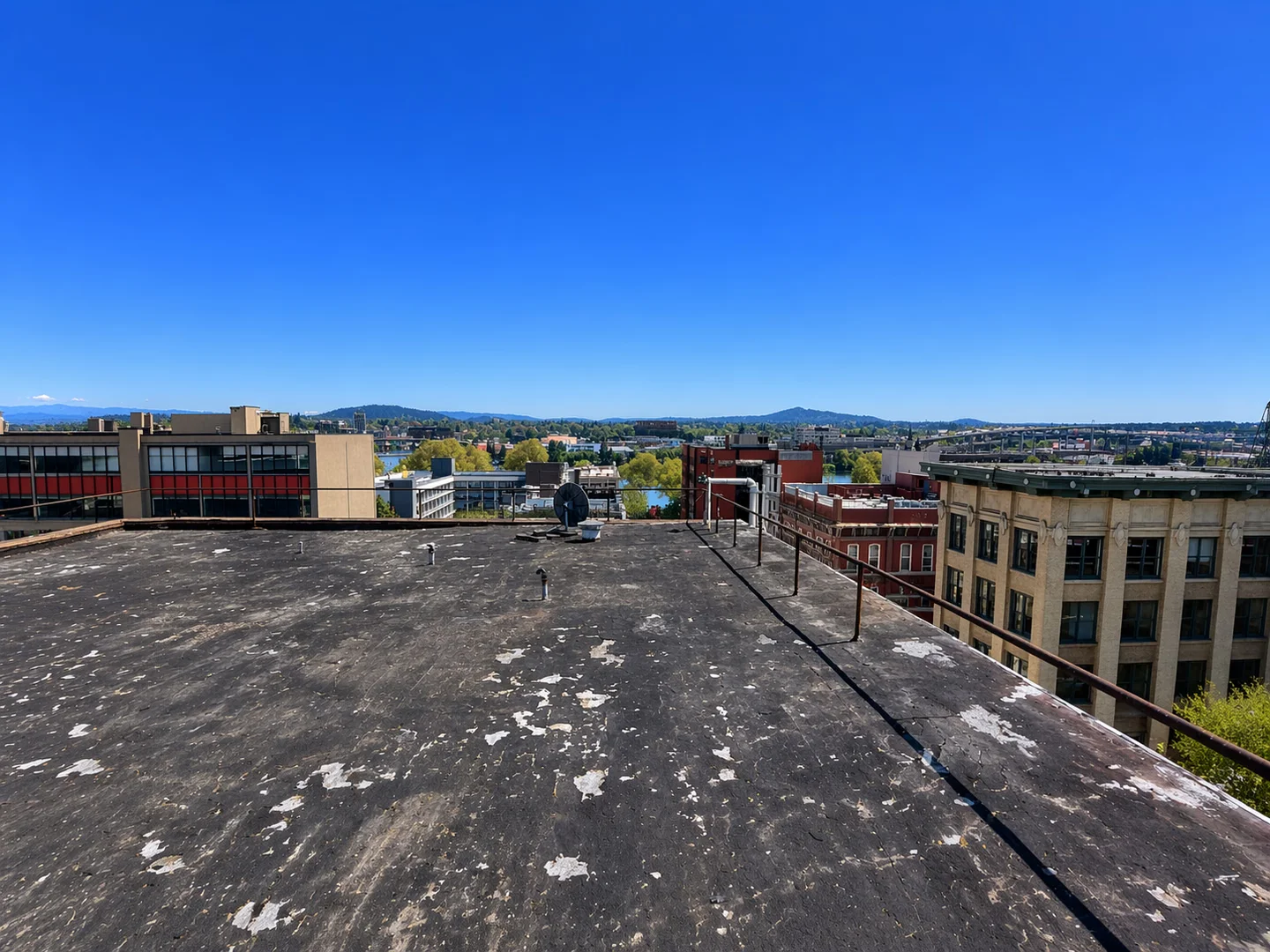 Weathered dark commercial roof with vents and a perimeter railing above surrounding buildings