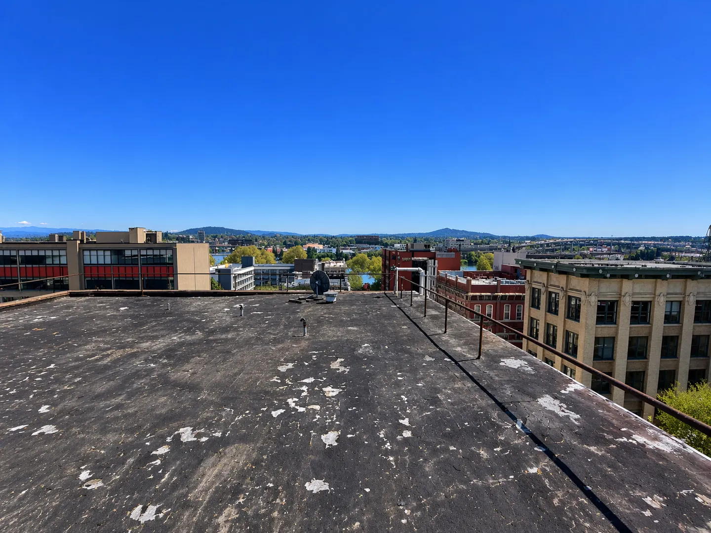 Weathered dark commercial roof with vents and a perimeter railing above surrounding buildings