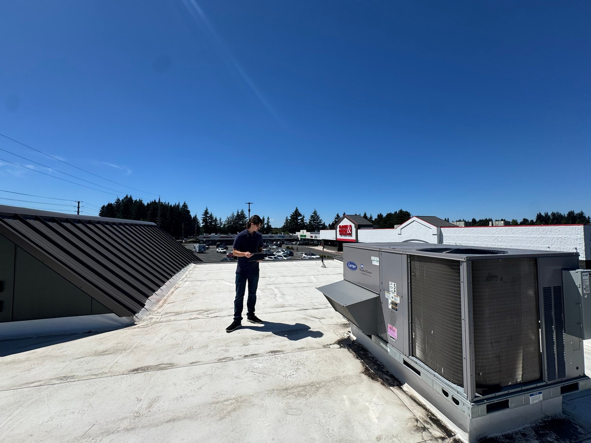Technician documenting a commercial flat roof beside rooftop equipment