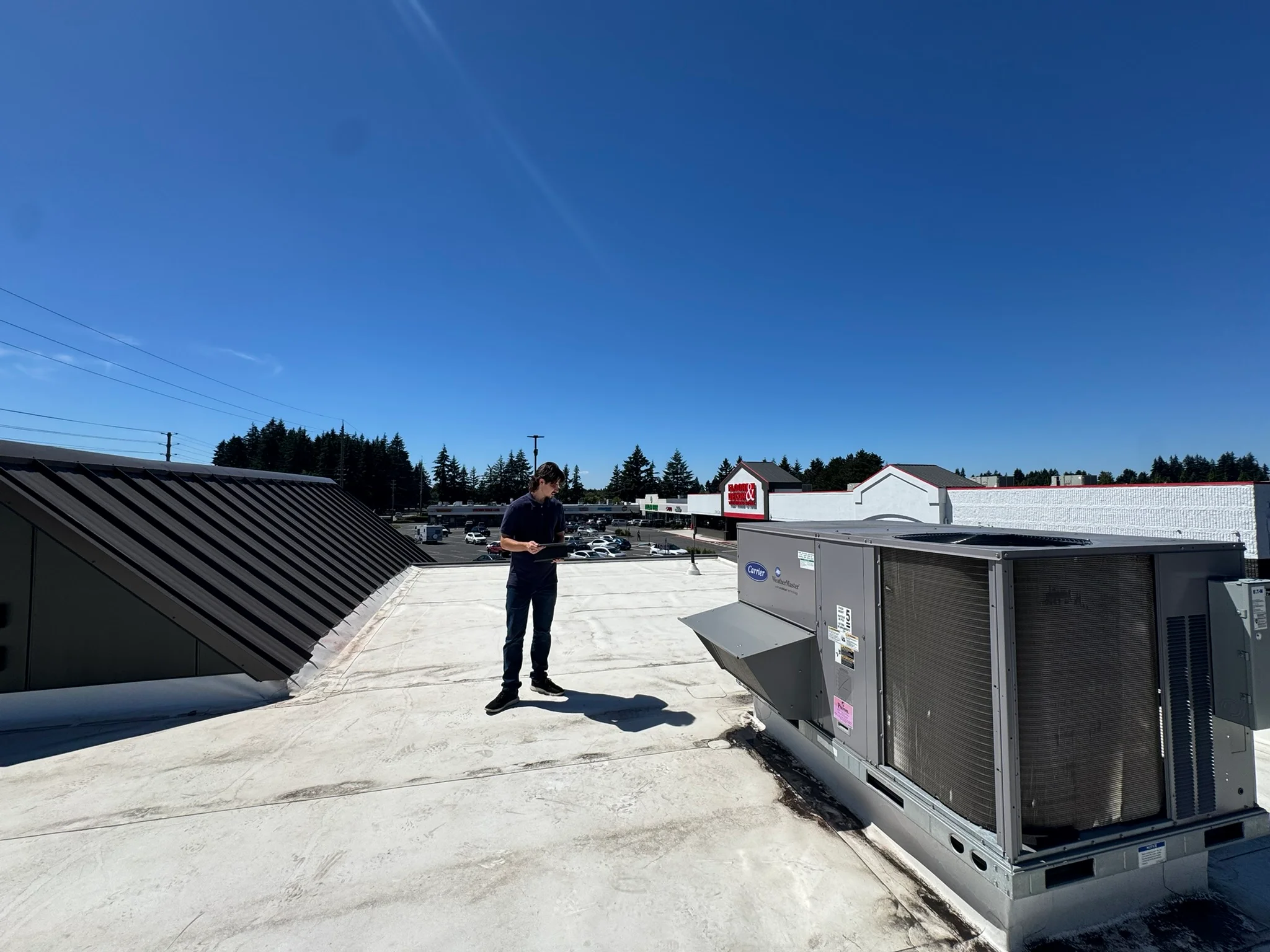 Inspector holding a tablet on a flat roof beside rooftop heating and cooling equipment