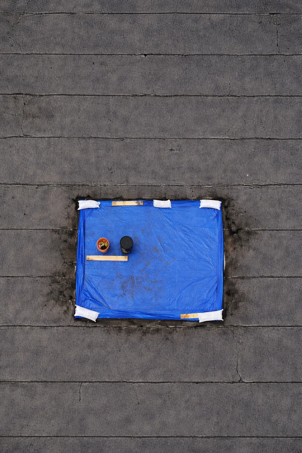 A blue tarp weighted with sandbags over a leak on a flat commercial roof, seen from above