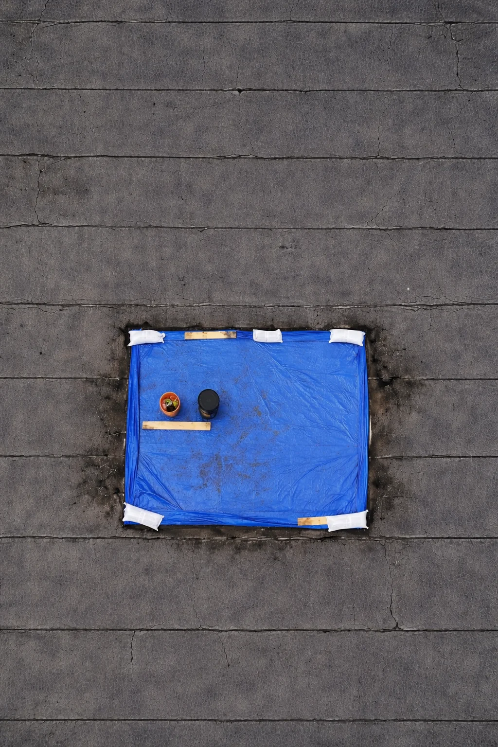 A blue tarp weighted with sandbags over a leak on a flat commercial roof, seen from above