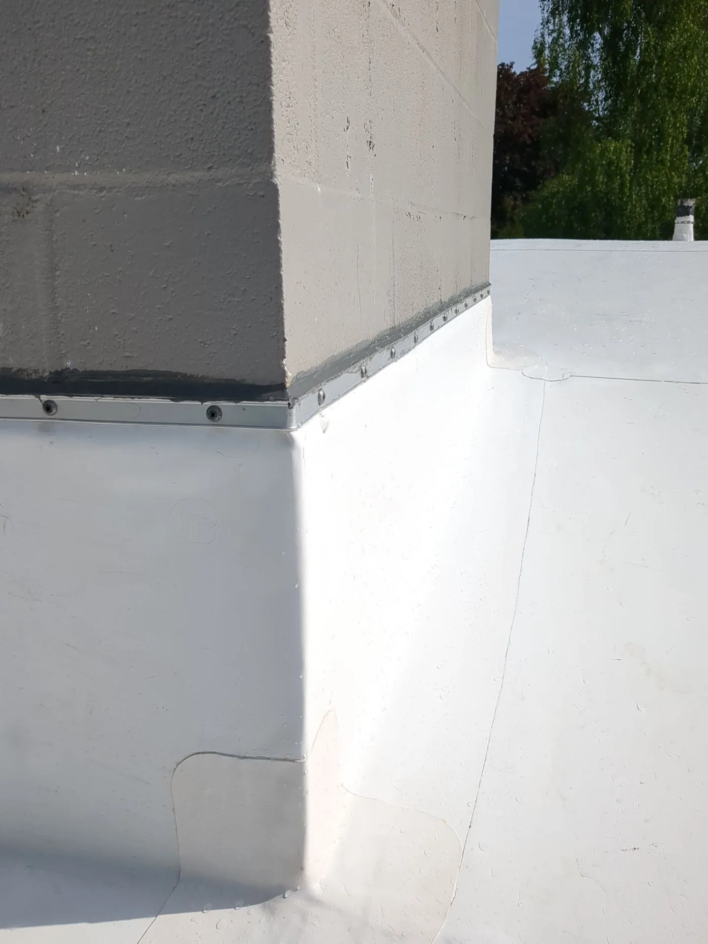 White roof membrane turned up a concrete block wall, held along its top edge by a screwed metal termination bar with a bead of sealant between the bar and the wall