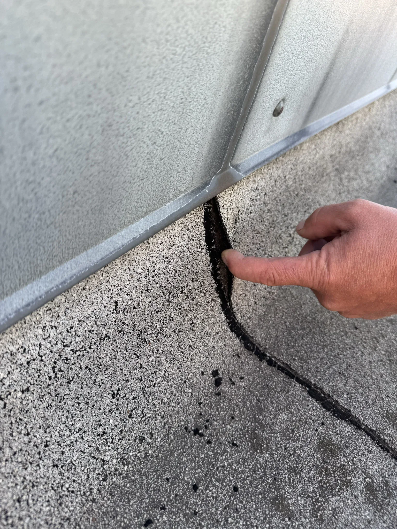 An inspector points to an open roofing joint below a metal edge
