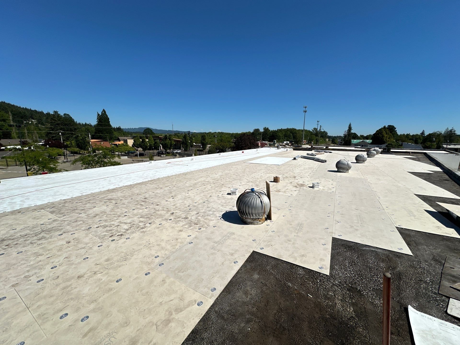 A roof mid-reroof with the old surface, new cover board, and finished white membrane side by side