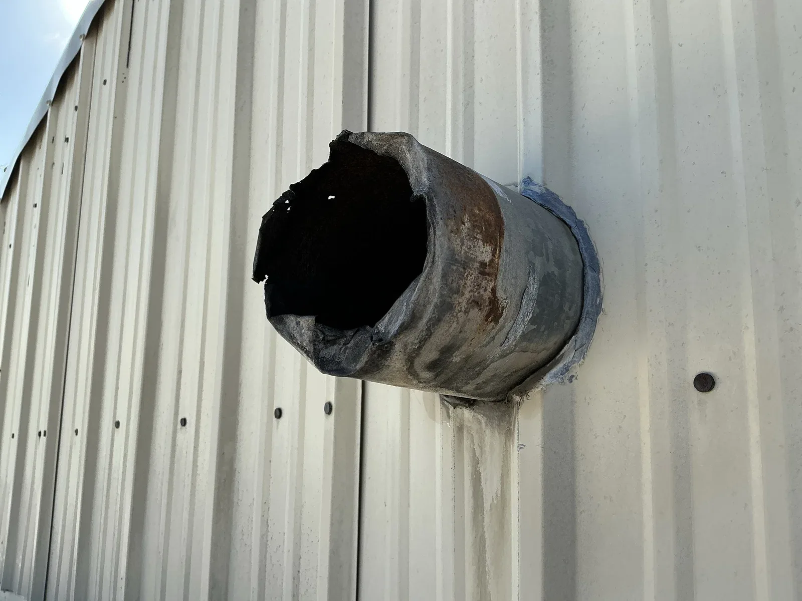 A short corroded pipe with a damaged open end projecting from a metal wall.