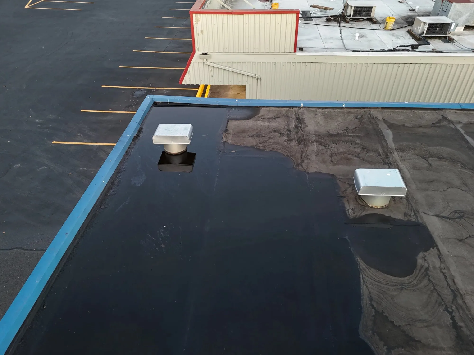 Water pooled across a corner of a flat roof, around two roof vents.
