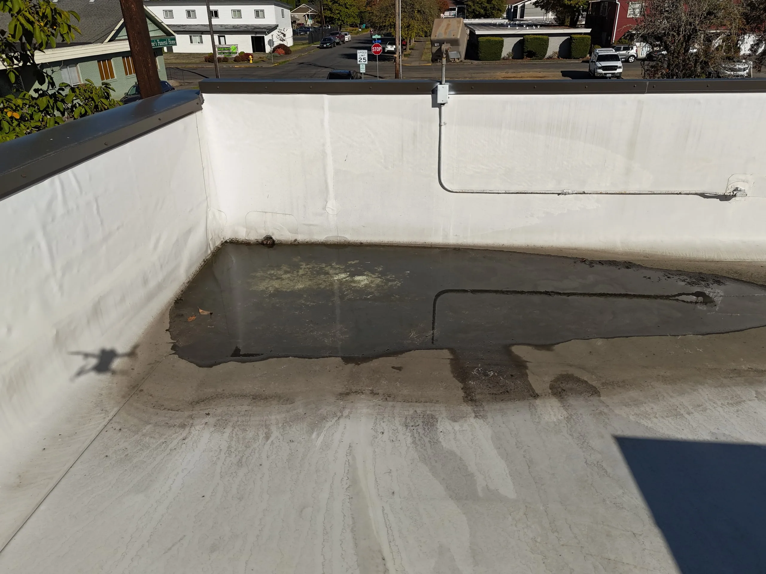 A wide puddle of standing water against the white wall of a flat roof, seen from a drone.