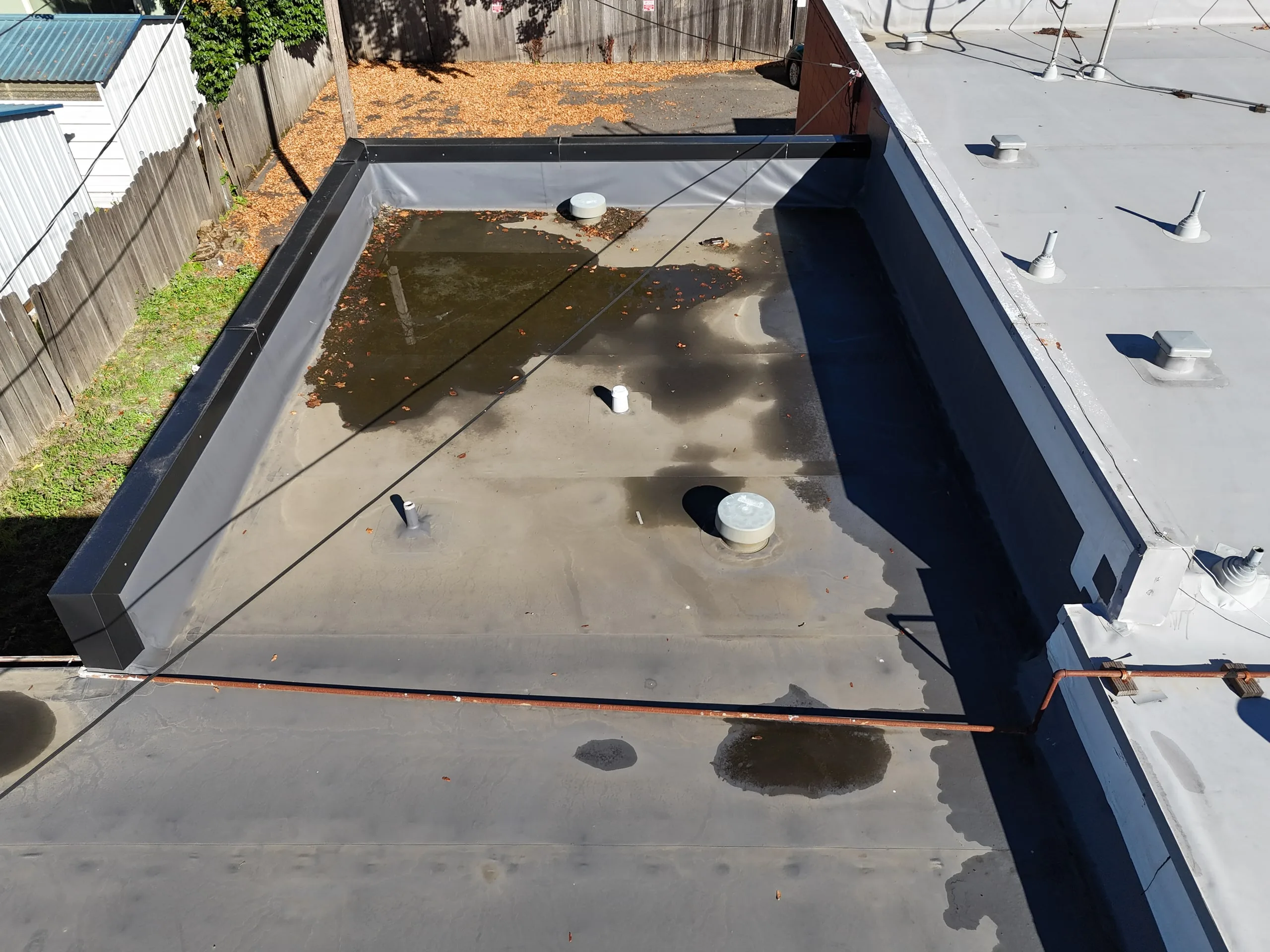 A drone view of a small flat roof inside a low wall, with puddles standing around its vents.