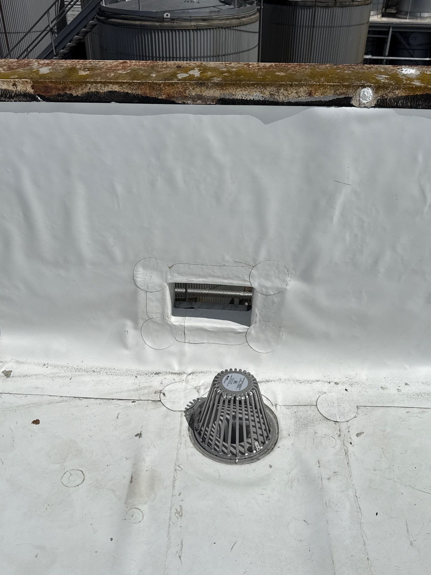 A new roof drain and a flashed scupper at the parapet of a white membrane roof