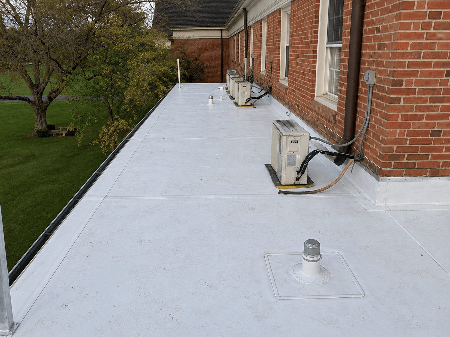 A new white roof membrane around vents and air conditioning units beside a brick building