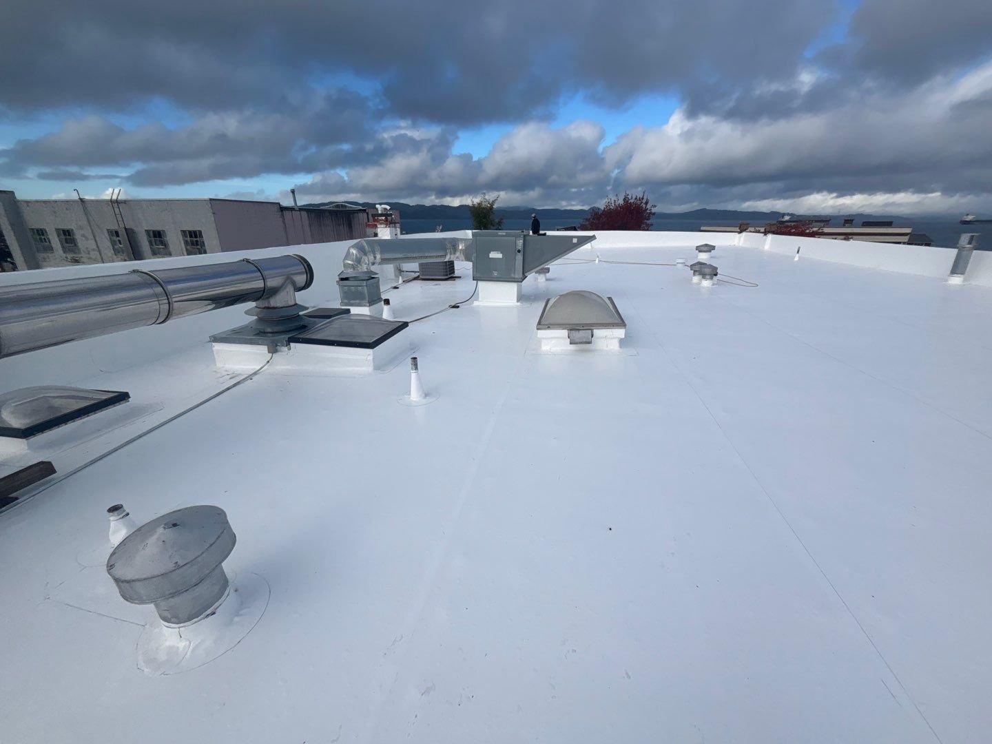 A commercial flat roof resealed in bright white silicone under a broken storm sky