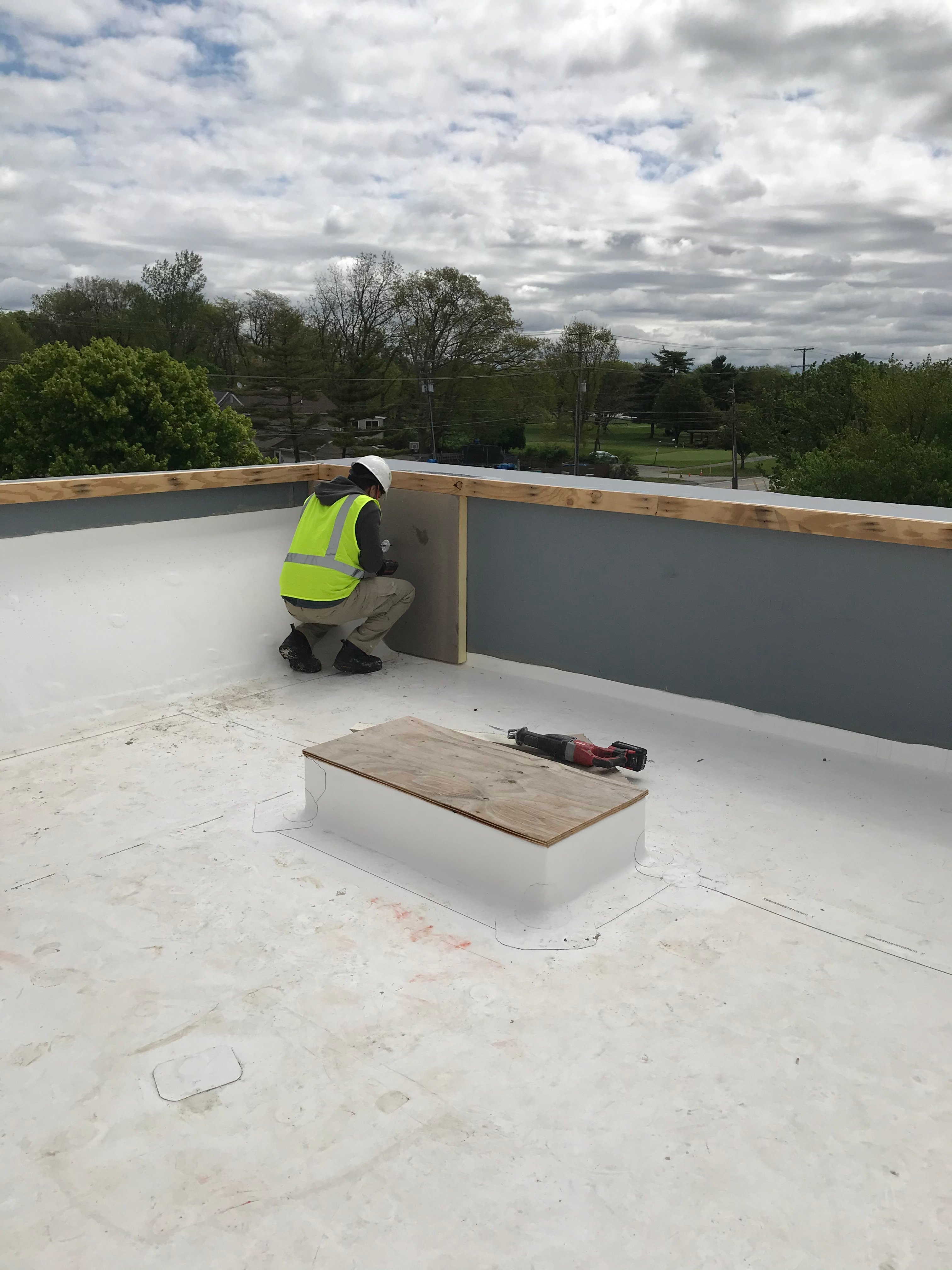 A roofer working on a parapet wall on a white commercial flat roof
