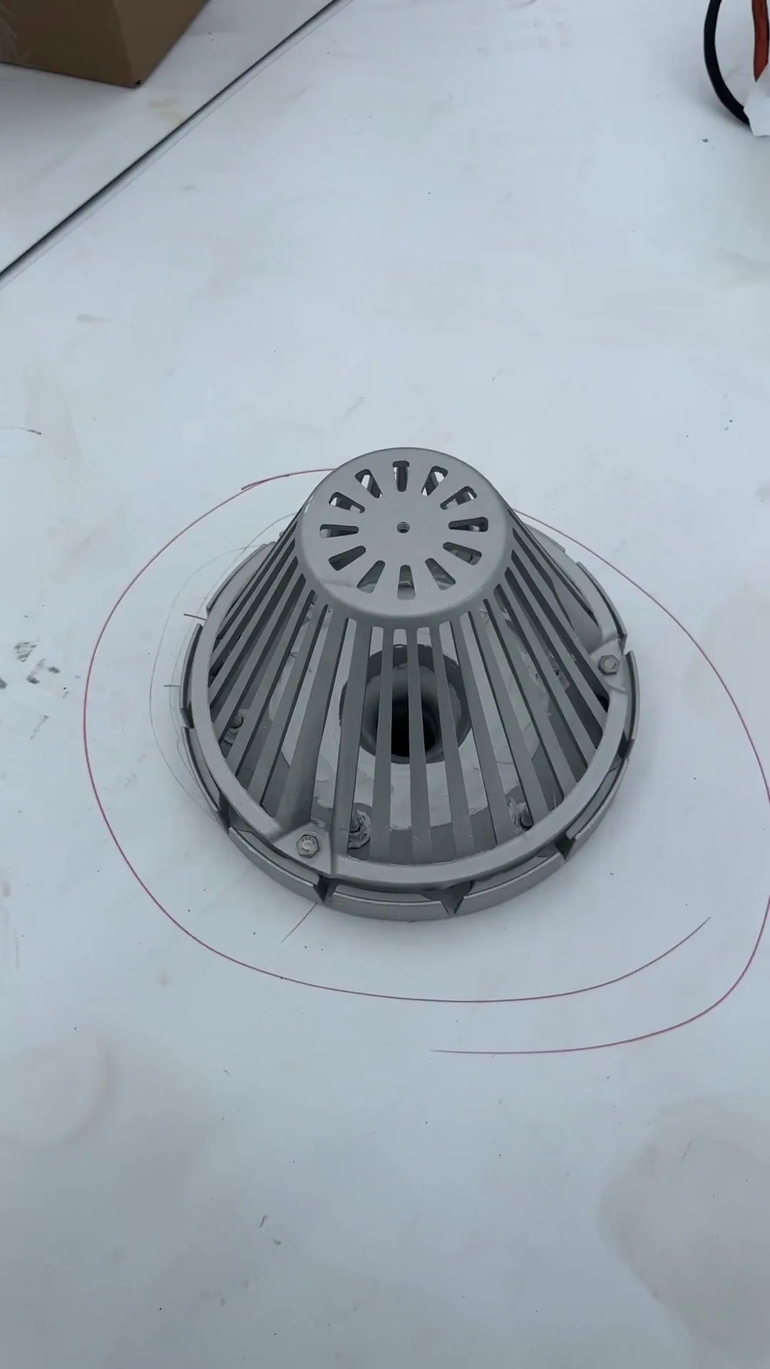 A roof drain on a white single-ply roof: a grey metal strainer dome sitting on a clamping ring held down by bolts, with the white membrane running under the ring into the drain