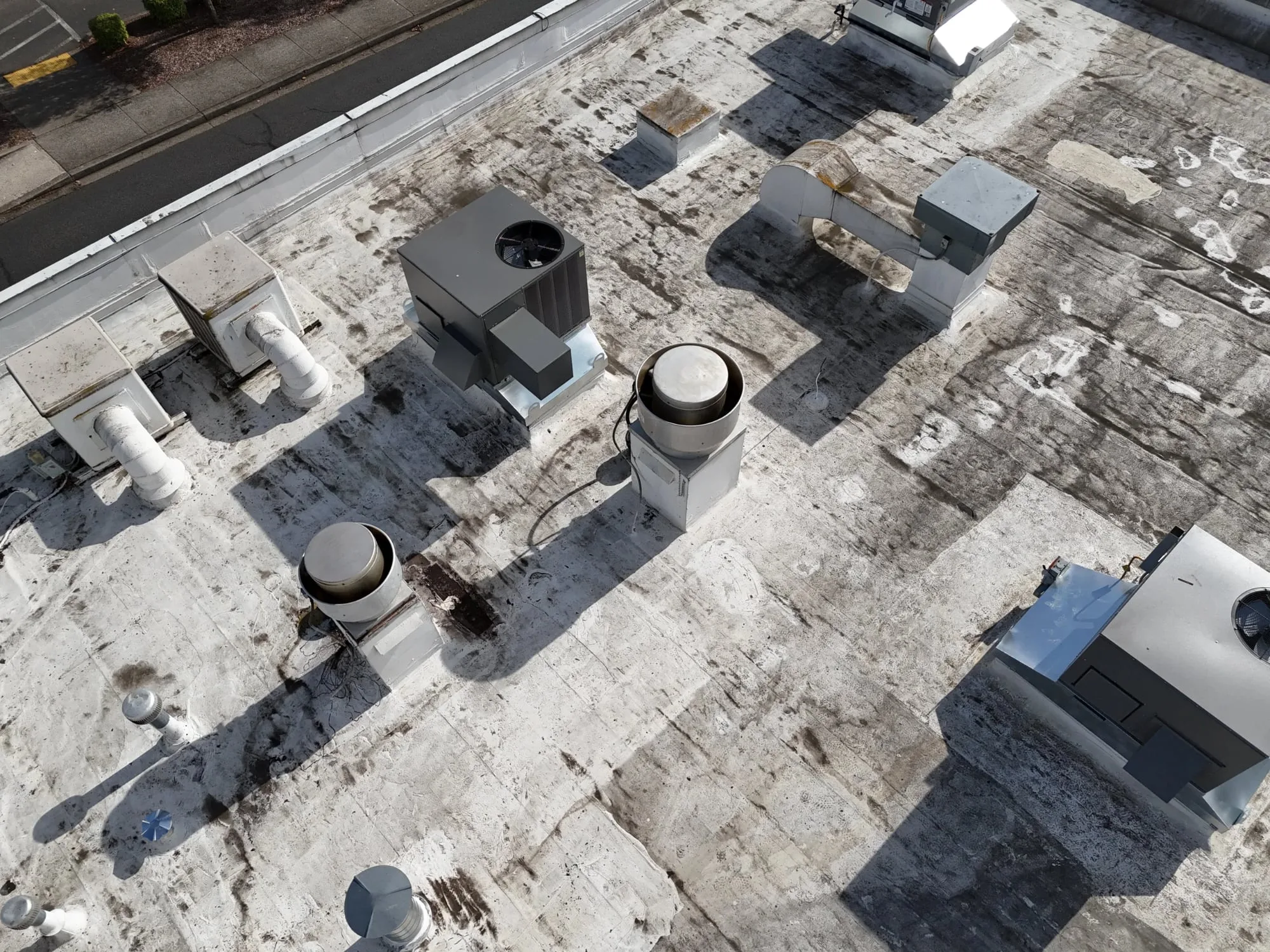 A flat roof seen from above, crowded with HVAC units, exhaust fans, vents, and pipes.