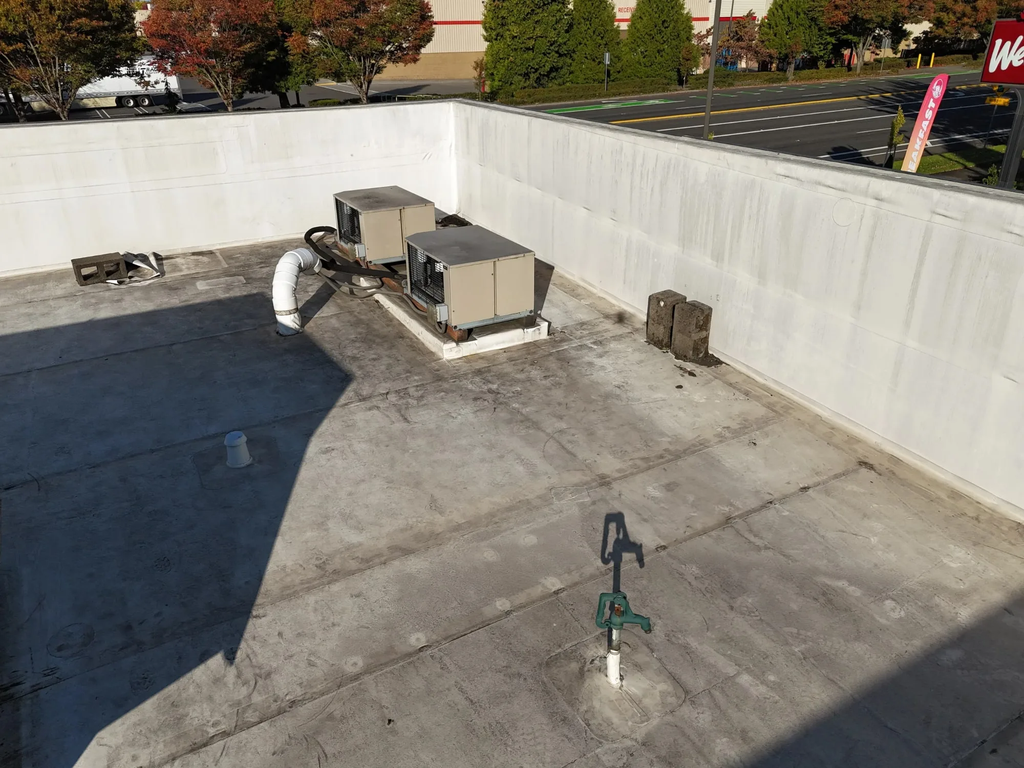 Two rooftop units and a vent on a flat roof, inside a tall white wall.