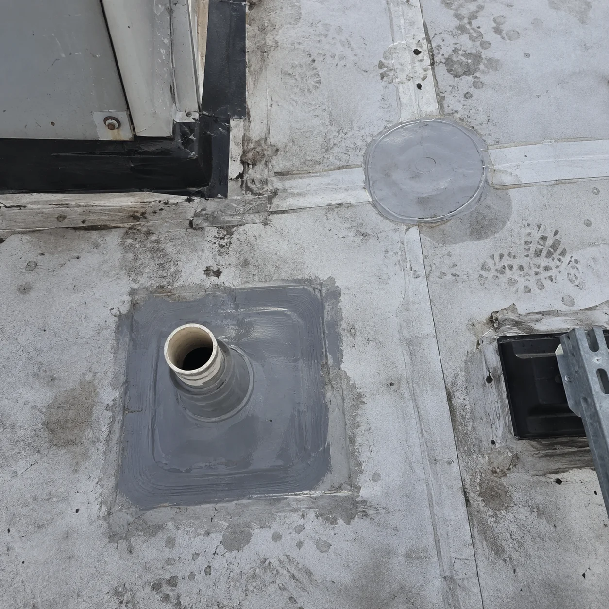 Sealed pipe penetration and patches on a white roof.