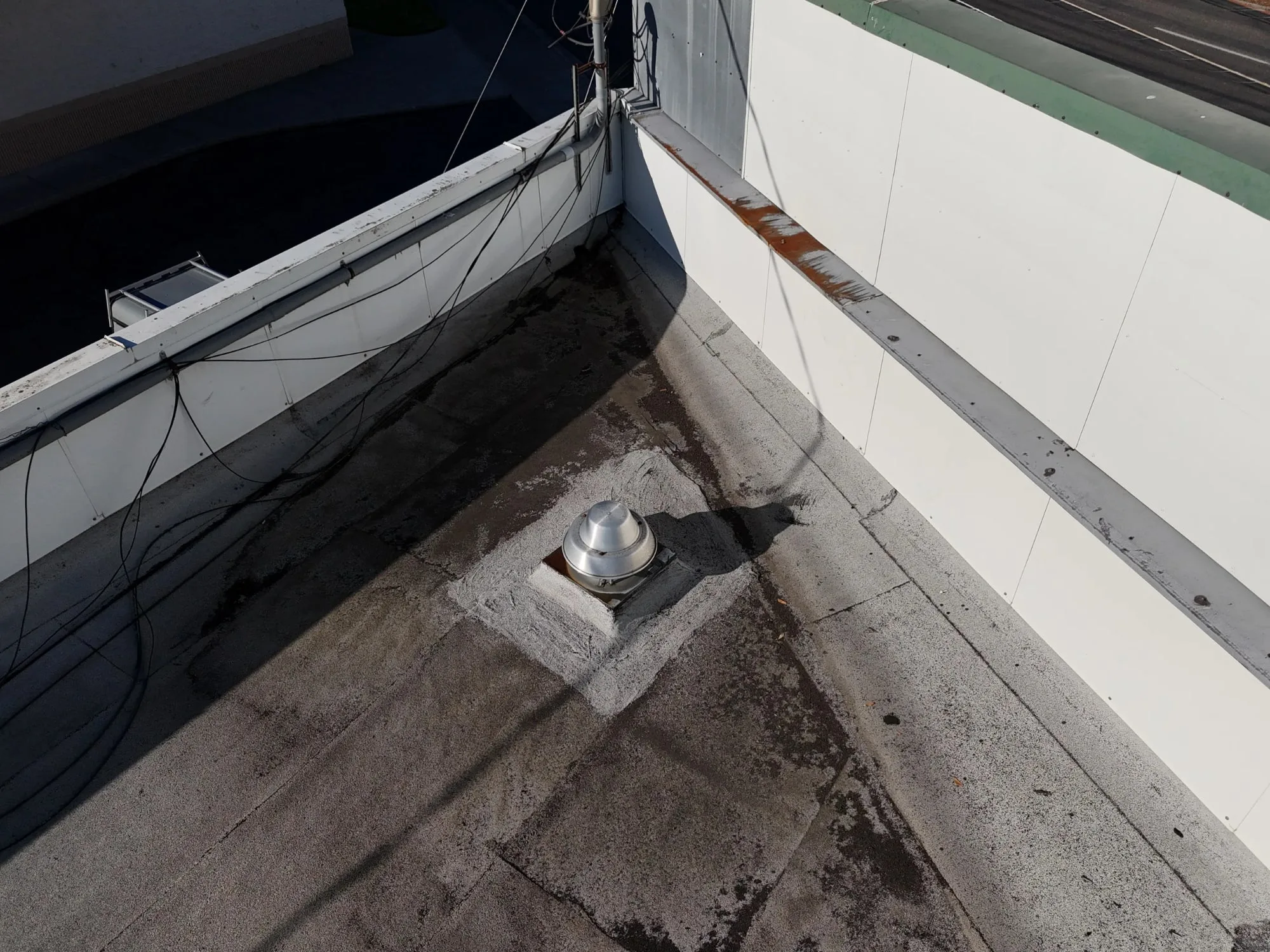 A roof vent on a flat roof, freshly sealed at its base.