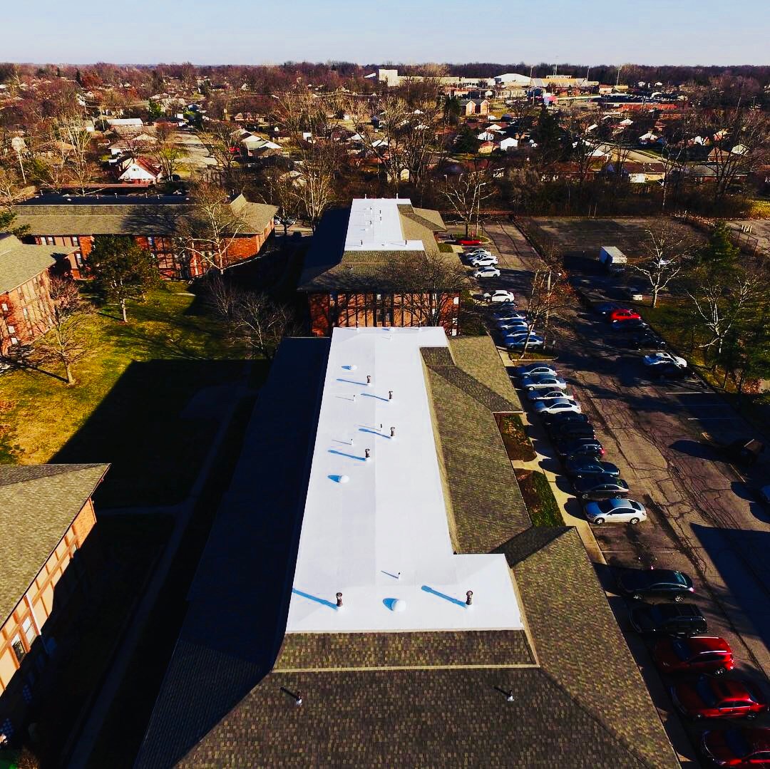 Drone view of an occupied building with a white resealed flat roof section and a full parking lot beside it