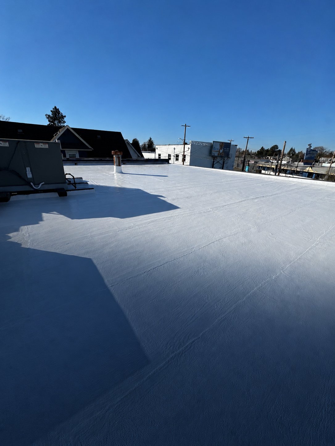 A clean, empty white silicone roof with a coated vent stack and HVAC unit under a clear winter sky