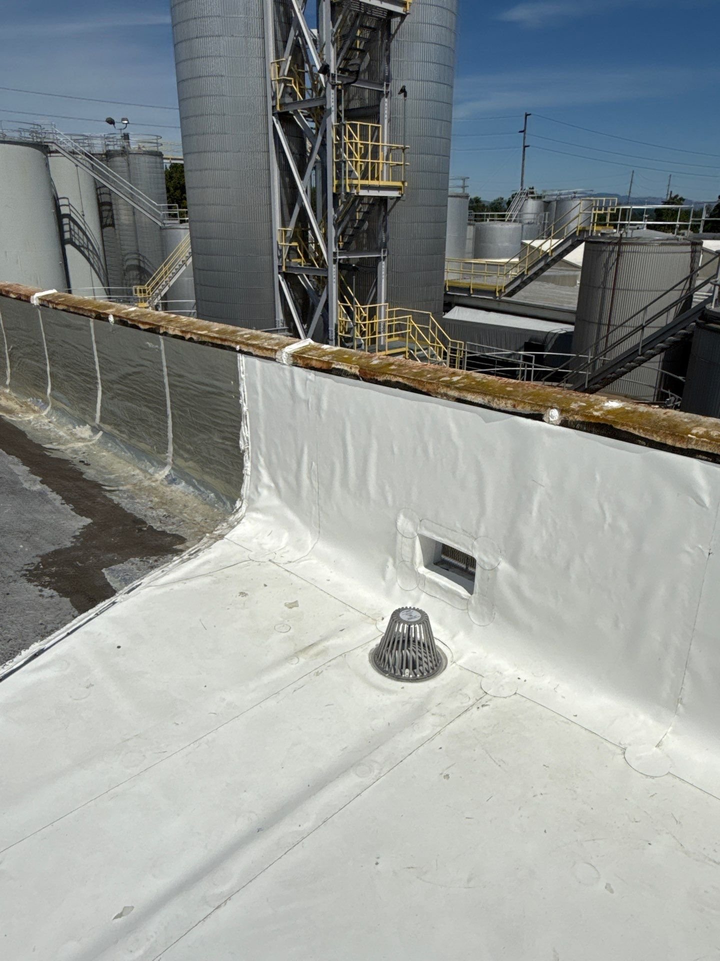 A low corner of a white silicone roof with a coated drain strainer and coated scupper against the parapet