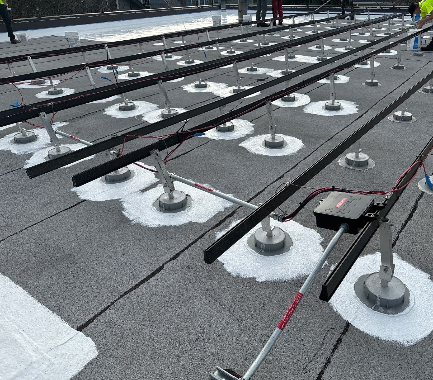 Rows of solar racking feet each sealed with white silicone on a commercial flat roof