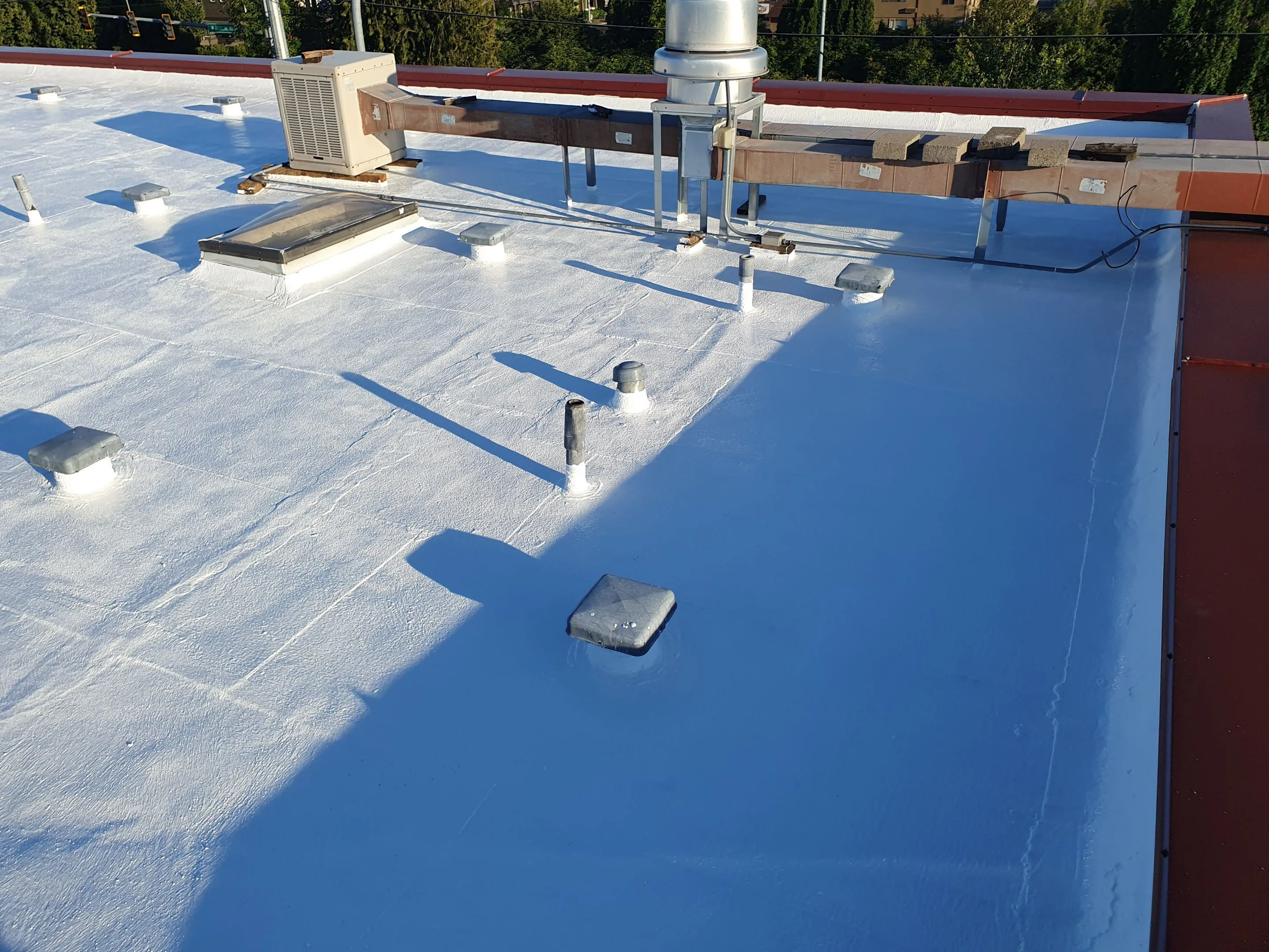 White-coated flat roof with vent pipes, low roof vents, a skylight, and elevated HVAC ductwork.