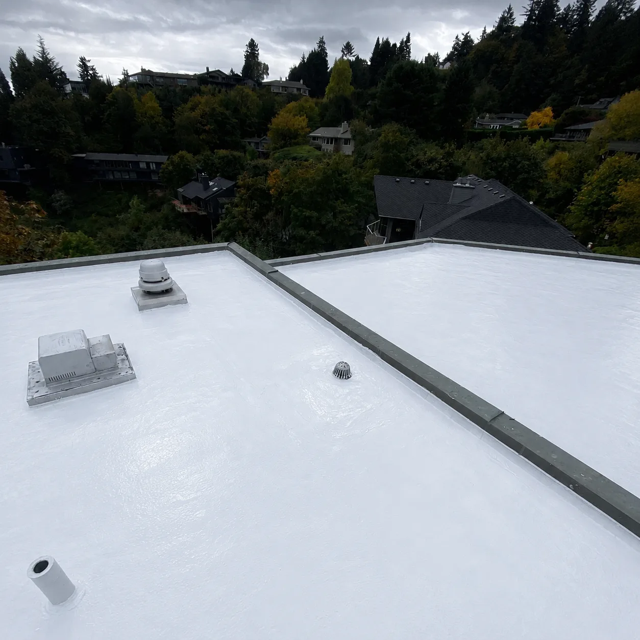 A flat roof freshly coated in white silicone, with a roof drain and vents.