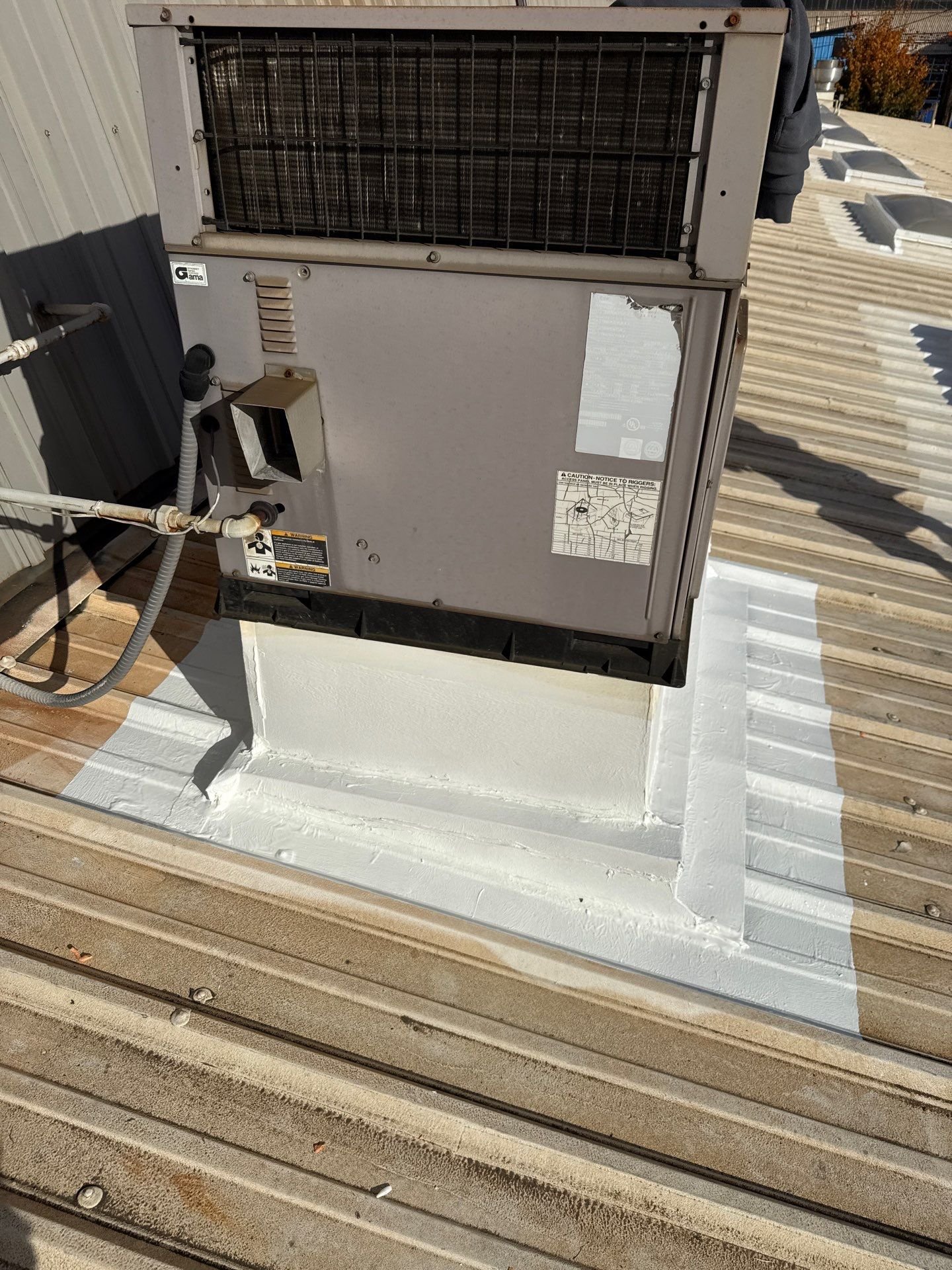 A rooftop HVAC curb and the surrounding metal roof seams sealed in white silicone