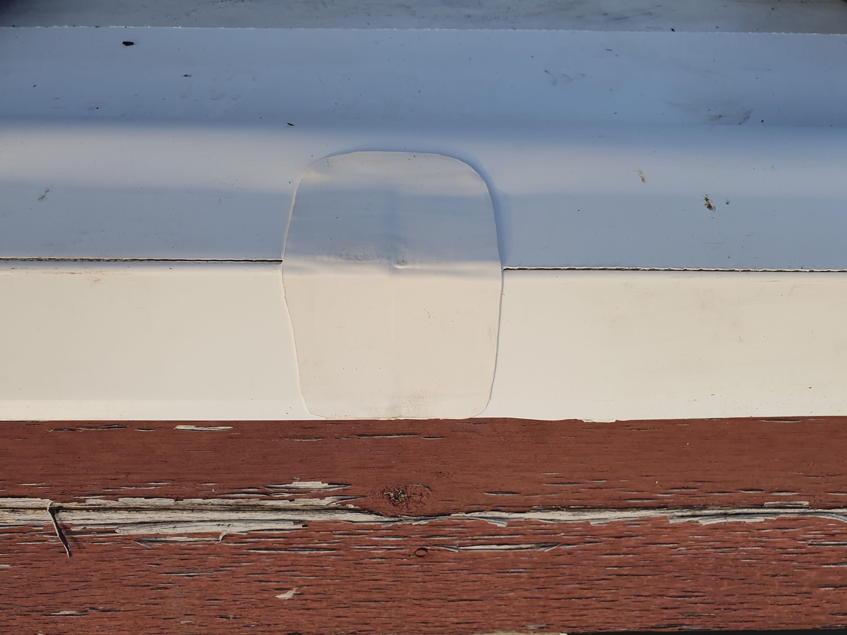 A failing membrane seam sealed under a smooth white silicone layer at a roof edge