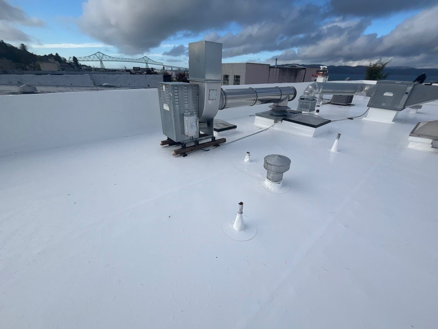 A large white resealed flat roof with coated vents and rooftop equipment under dramatic clouds