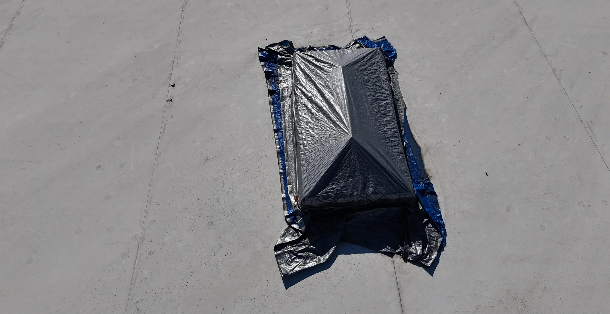A skylight on a white flat roof, covered with a tarp to hold off the leak until it can be sealed.
