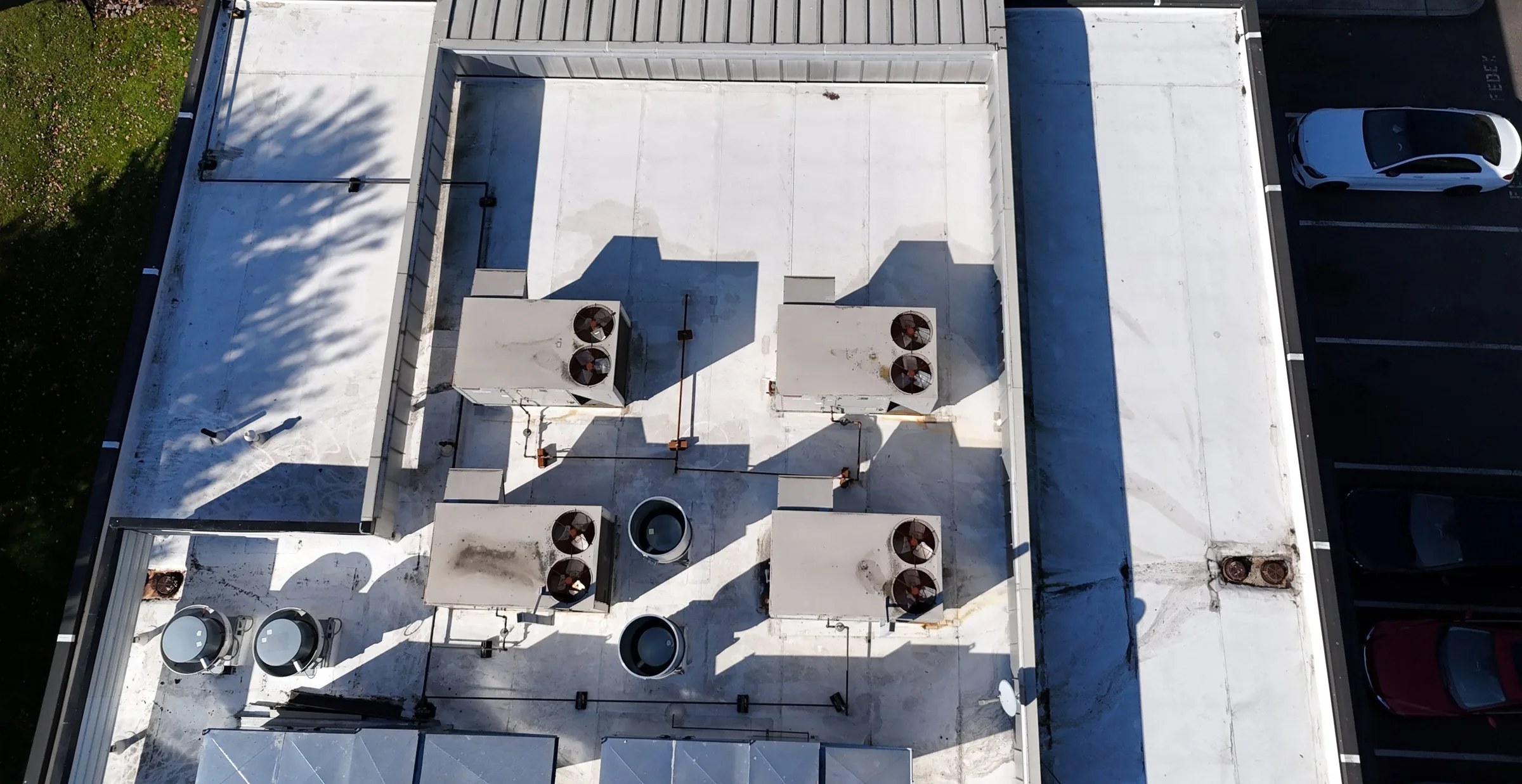 A clean white flat roof seen from straight above, with four rooftop units in the middle and parked cars alongside.