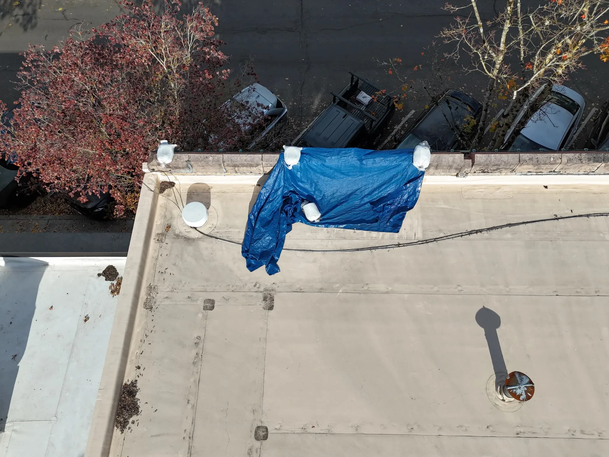 A blue tarp blown loose from a parapet on a flat roof, held by sandbags.