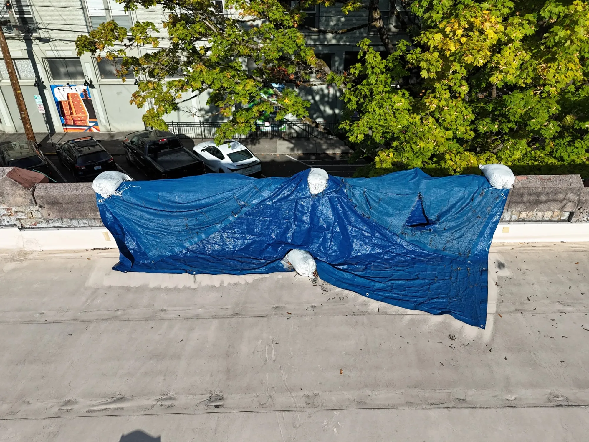 A blue tarp weighed down with sandbags over a leaking parapet on a flat roof.