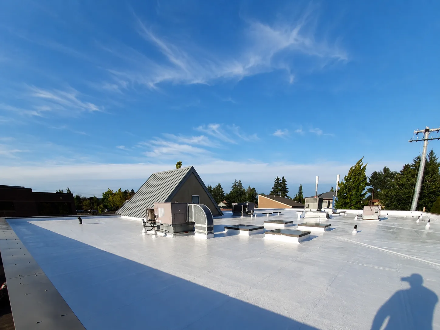 White-coated low-slope roof surrounding rooftop HVAC equipment, skylights, and vent pipes.