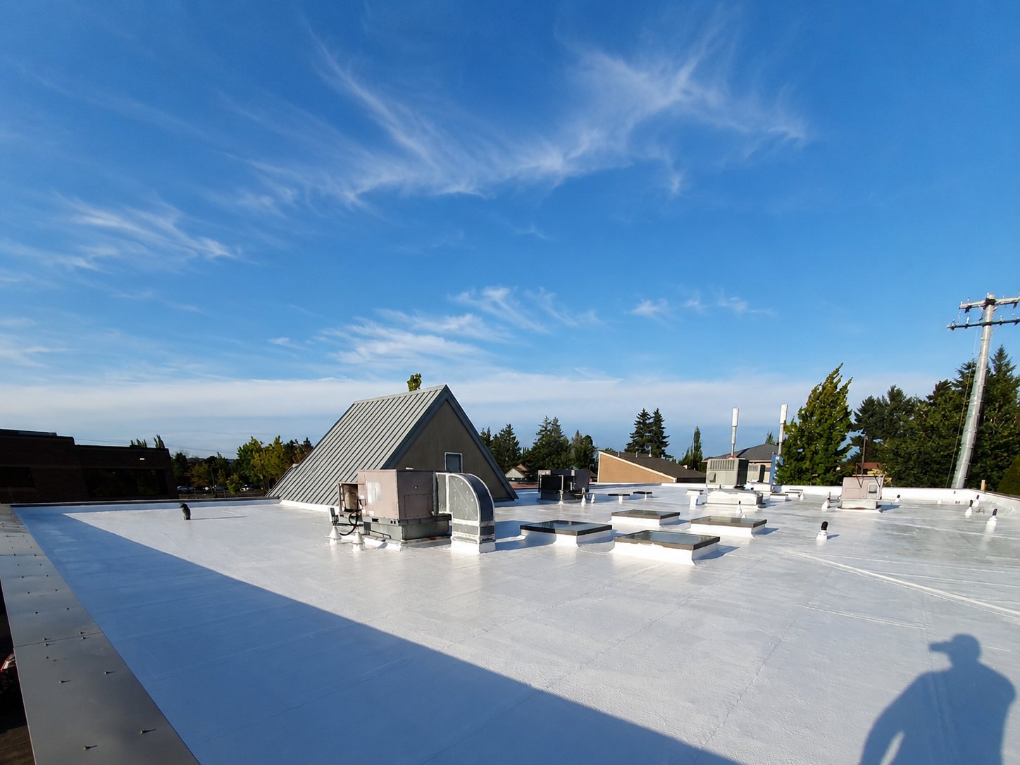 A finished white silicone flat roof stretching to the parapet under a clear sky