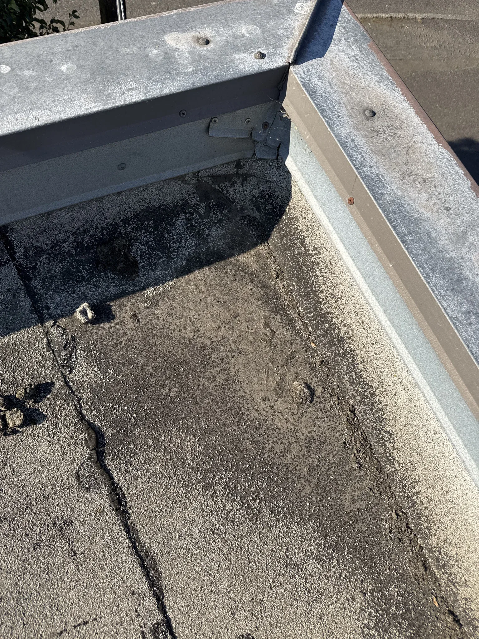 Worn asphalt roofing and an open joint beneath a metal roof corner