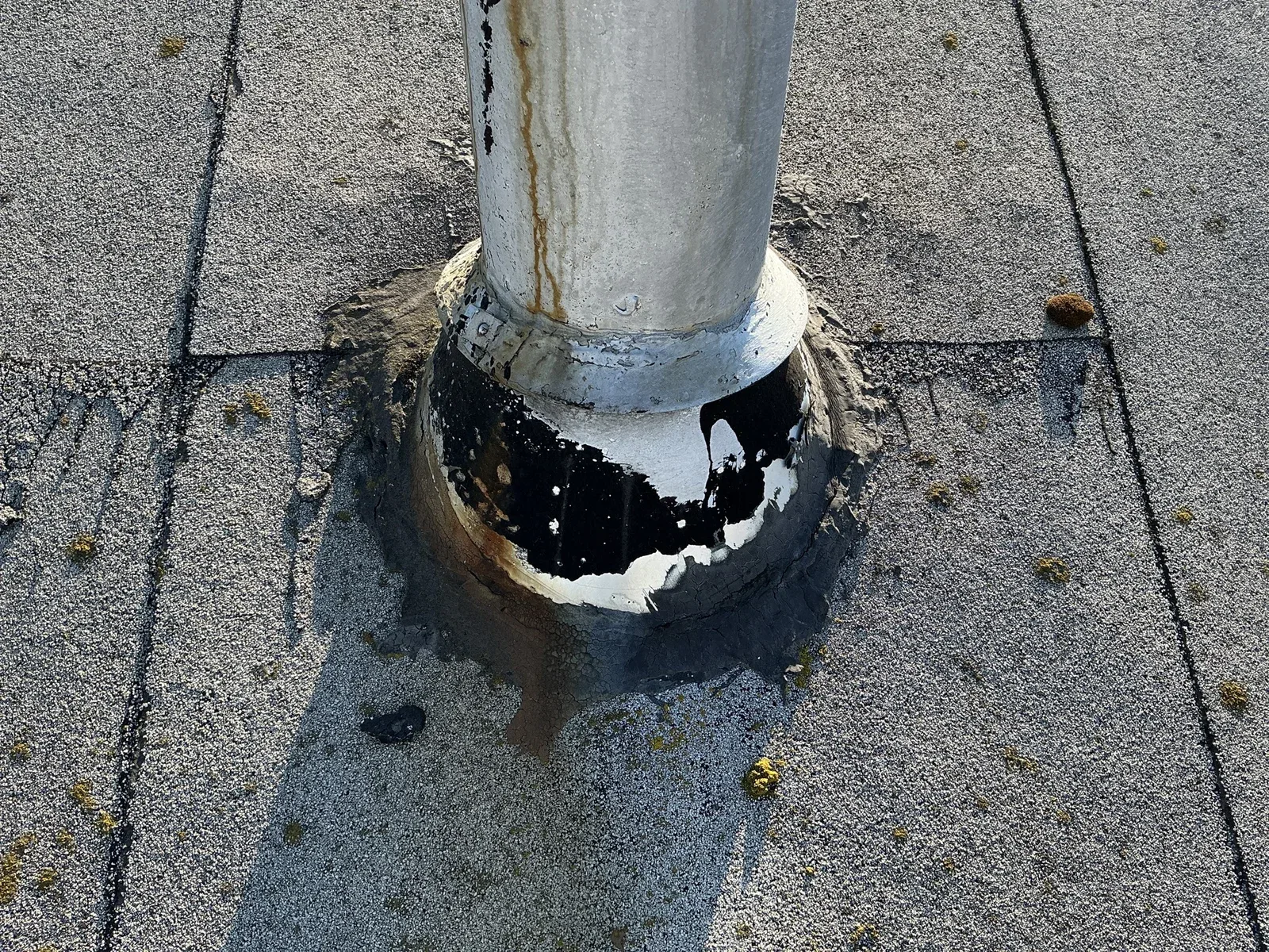 A roof pipe with peeling finish and cracked sealing material around its base.
